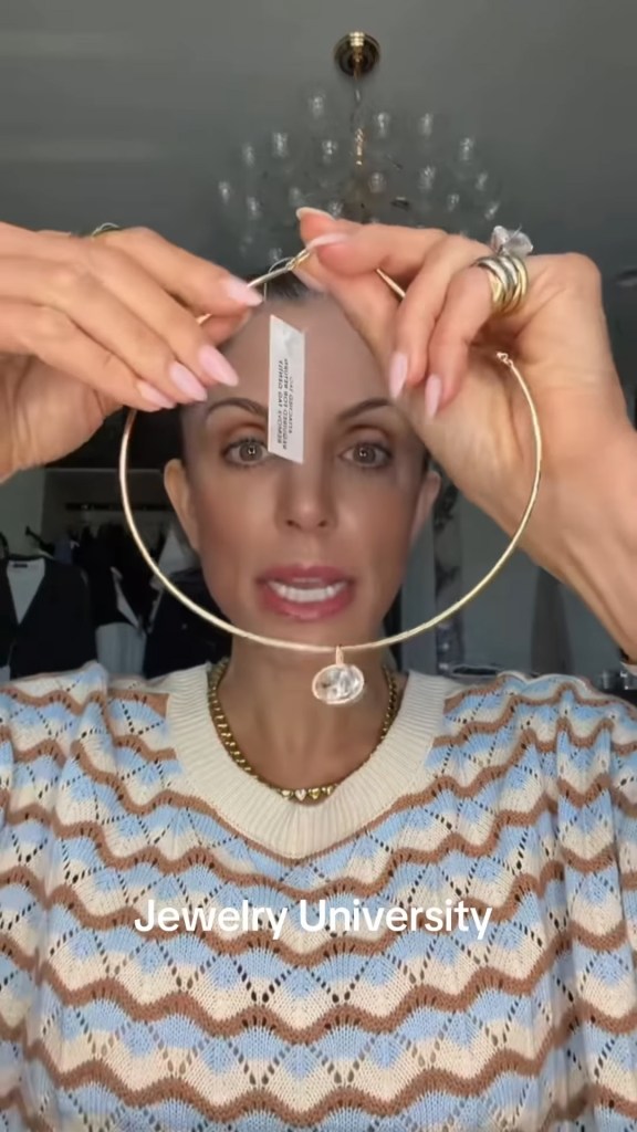 Bethenny Frankel holding up a gold necklace with a clear pendant.