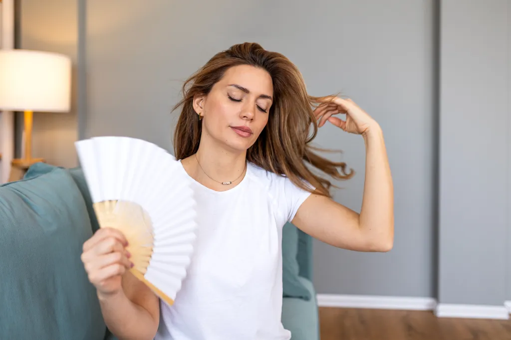 Young woman with closed eyes using a white hand fan to cool down.