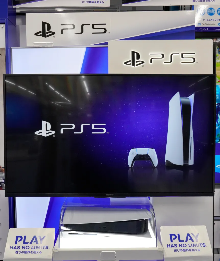 A PlayStation 5 console and controller displayed on a screen above a physically showcased PlayStation 5 console.