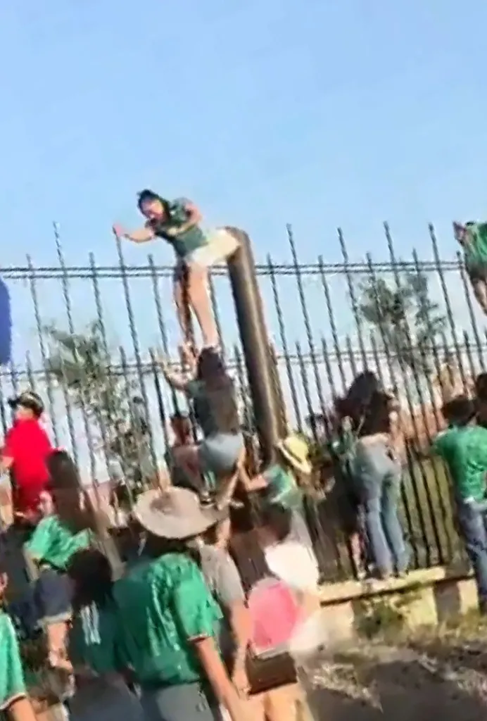People climbing over a fence and a pole.