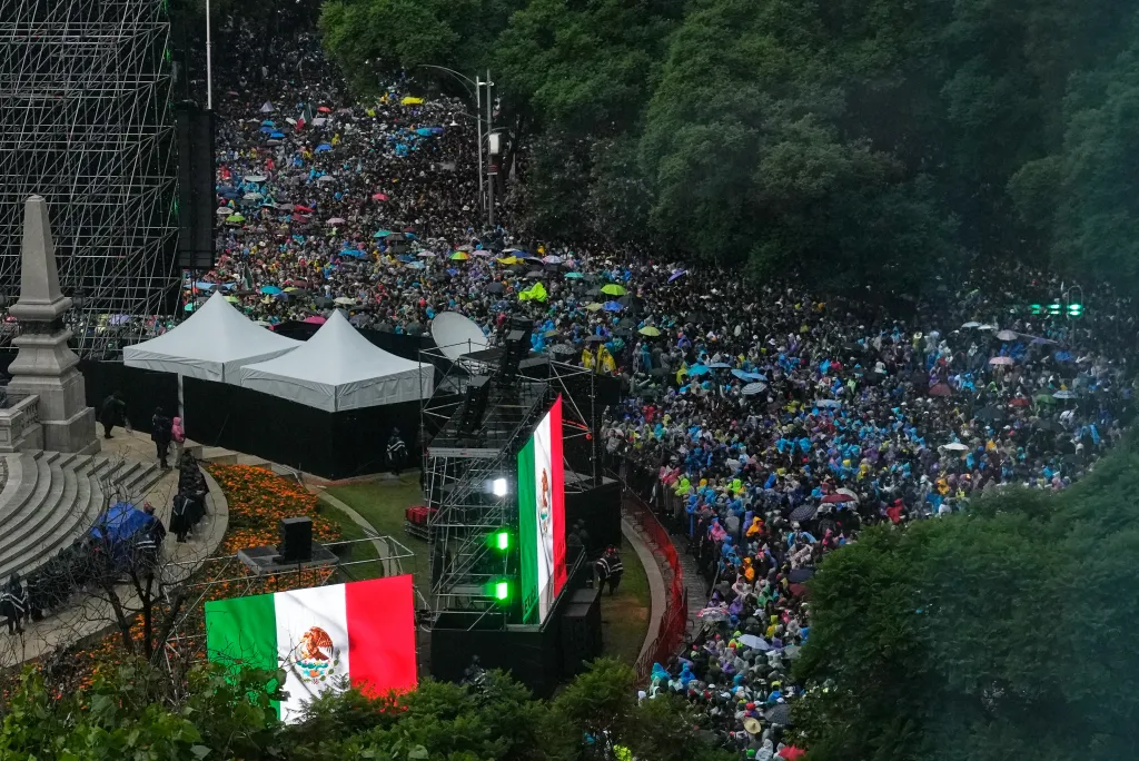 A large crowd of people with colorful umbrellas gathered, with large Mexican flags on display.