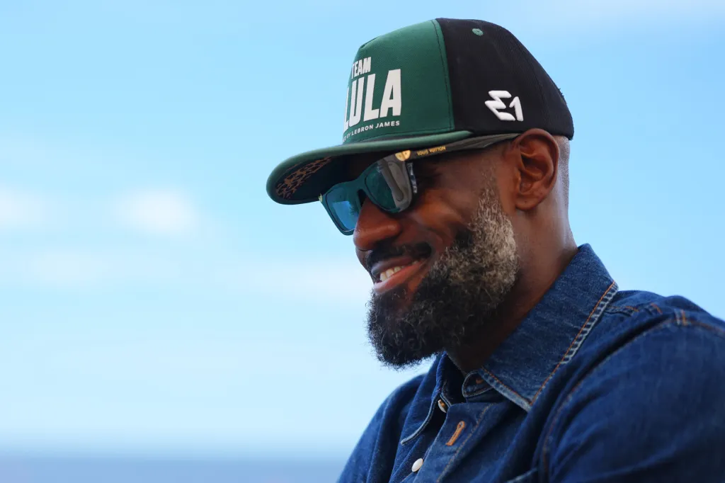 LeBron James wearing a green and black "TEAM LULA" hat and sunglasses, smiling.